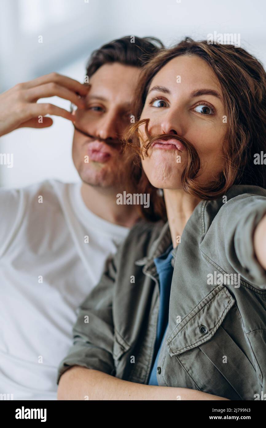 Gli sposi più felici giocano e si mettono in posa facendo i baffi con capelli ricci brunette e bacio sorridendo ampiamente per i selfie tramite il primo piano dello smartphone Foto Stock