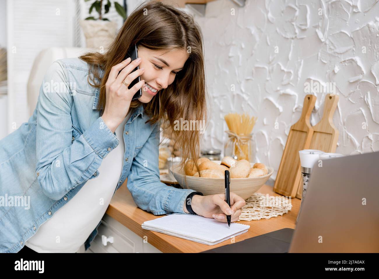 Ritratto di interessante freelance femminile parlare al telefono con un collega e registrare momenti di lavoro e utilizzando un computer portatile. Bella impresa Foto Stock