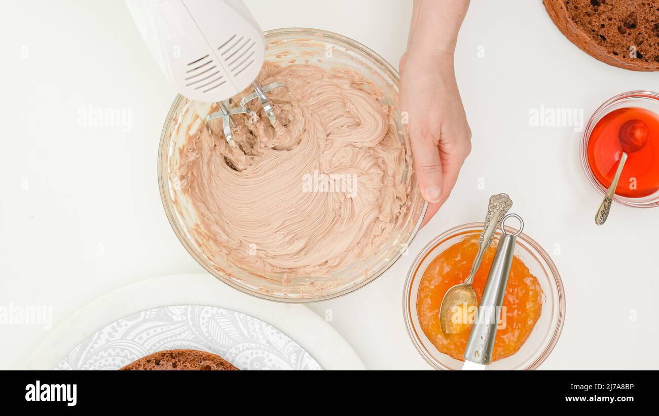 Le mani della donna mescolano la crema del burro usando un miscelatore elettrico. Ricetta passo passo per torta al cioccolato, primo piano ingredienti, piatto Foto Stock