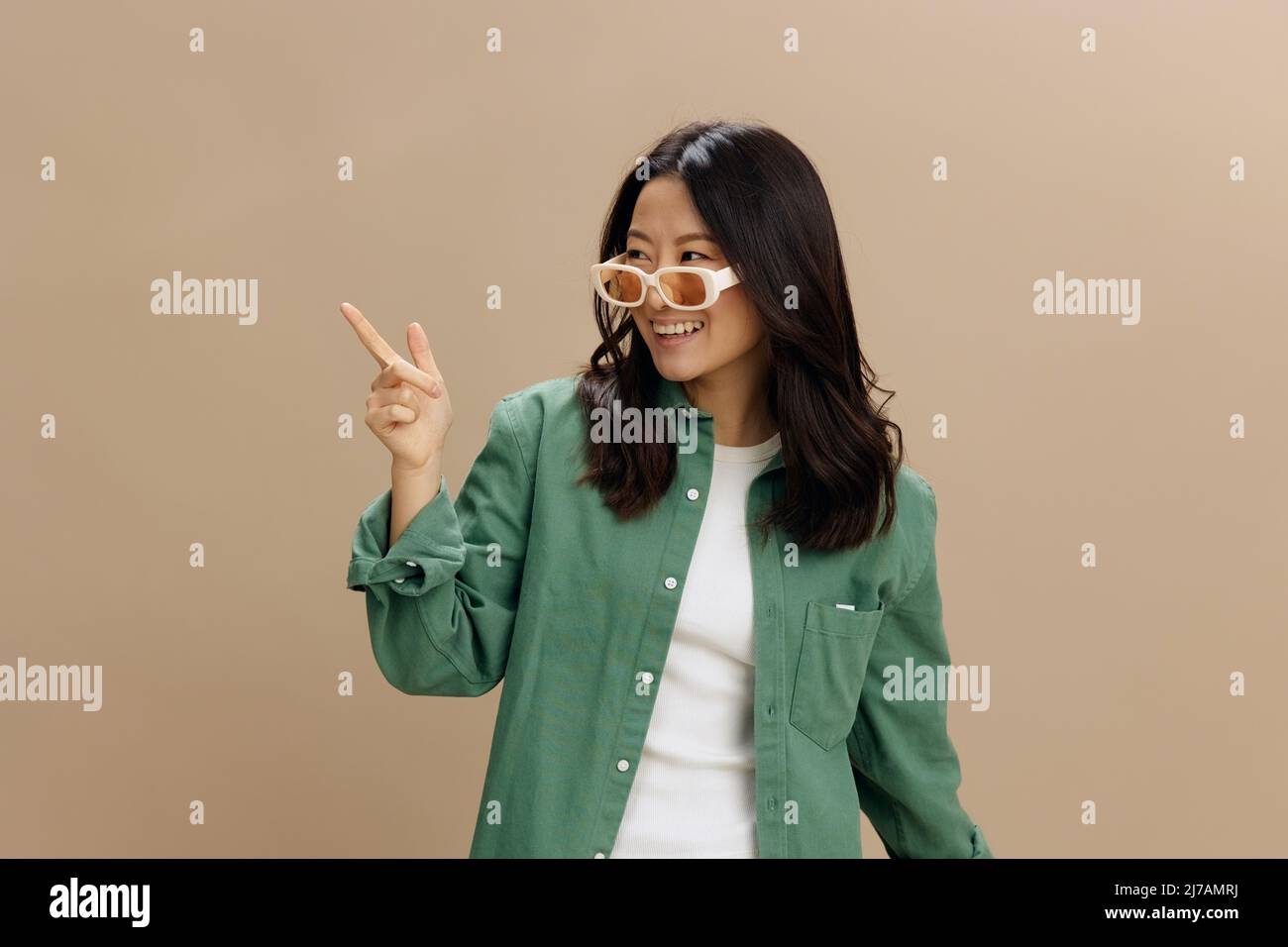 Ridendo felice coreano giovane donna in maglia verde kaki elegante eyewear  punta le dita da parte a copiare spazio in posa isolato su beige pastello  studio Foto stock - Alamy