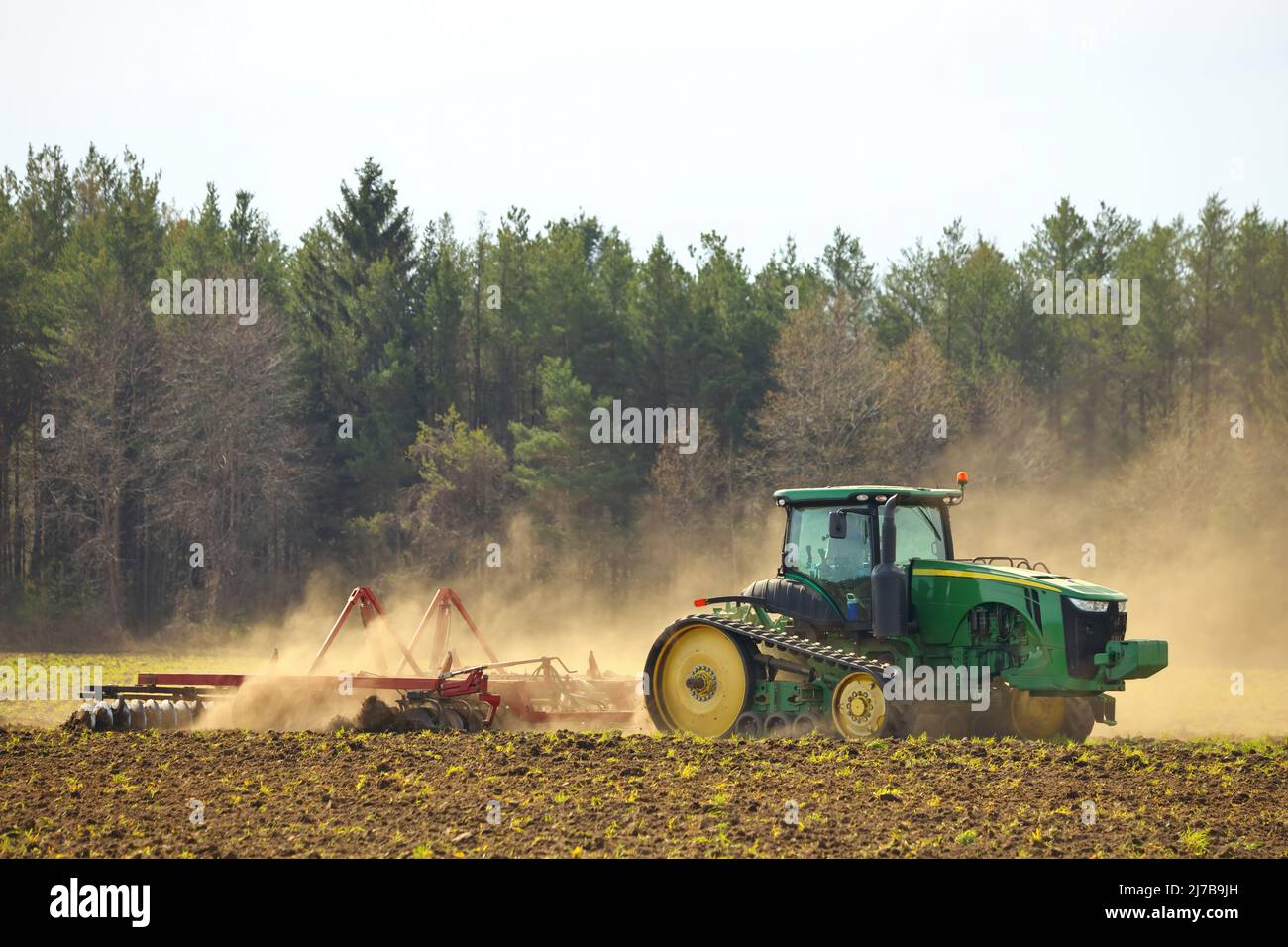 Trattore cingolato per arare il campo con erpice in primavera in azienda agricola con nubi di polvere Foto Stock