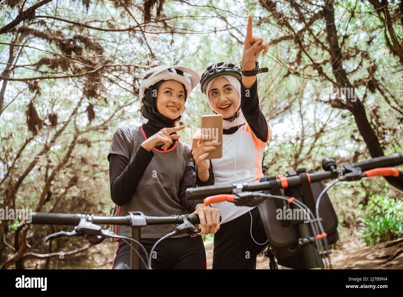 Due donne in bicicletta utilizzando un telefono cellulare che punta la strada Foto Stock