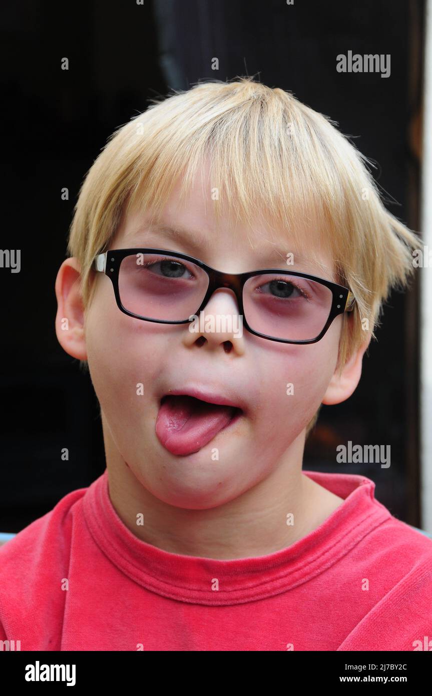 portait di un ragazzo giovane che indossa occhiali sulla testa attaccando la lingua fuori , concetto di essere stupido faccia buffa . Foto Stock