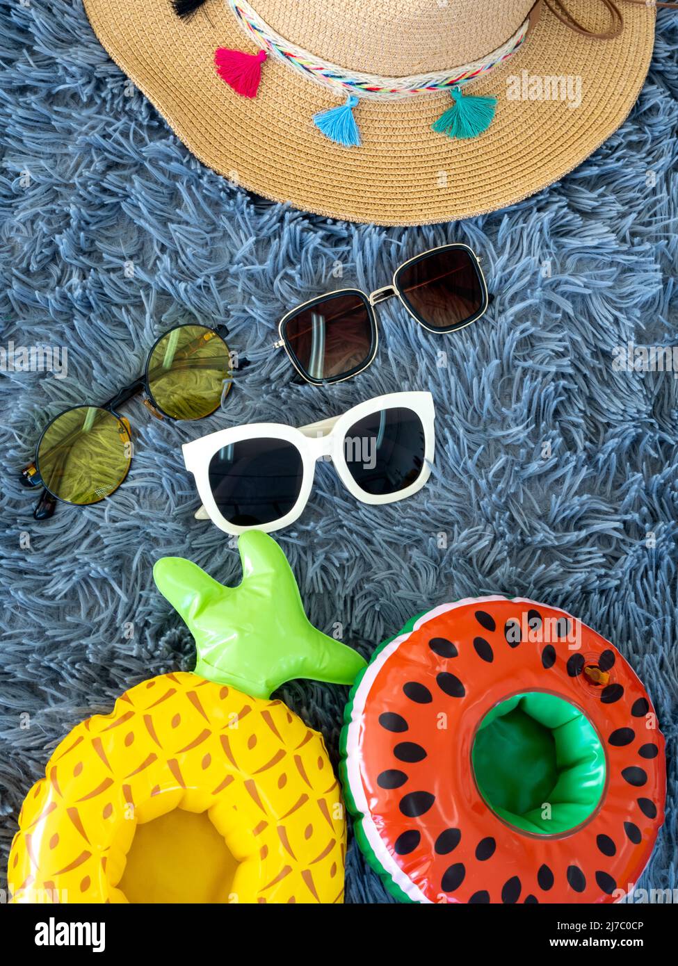 Spiaggia estate roba, tre occhiali da sole moda, carino donna cappello da spiaggia, cocomero e ananas gonfiabile buoy ring su sfondo tappeto, stile verticale Foto Stock