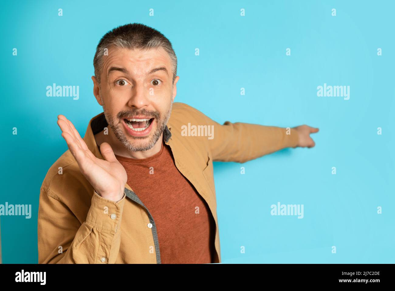 Uomo di età media puntando dito a lato di pubblicità offerta, sfondo blu Foto Stock