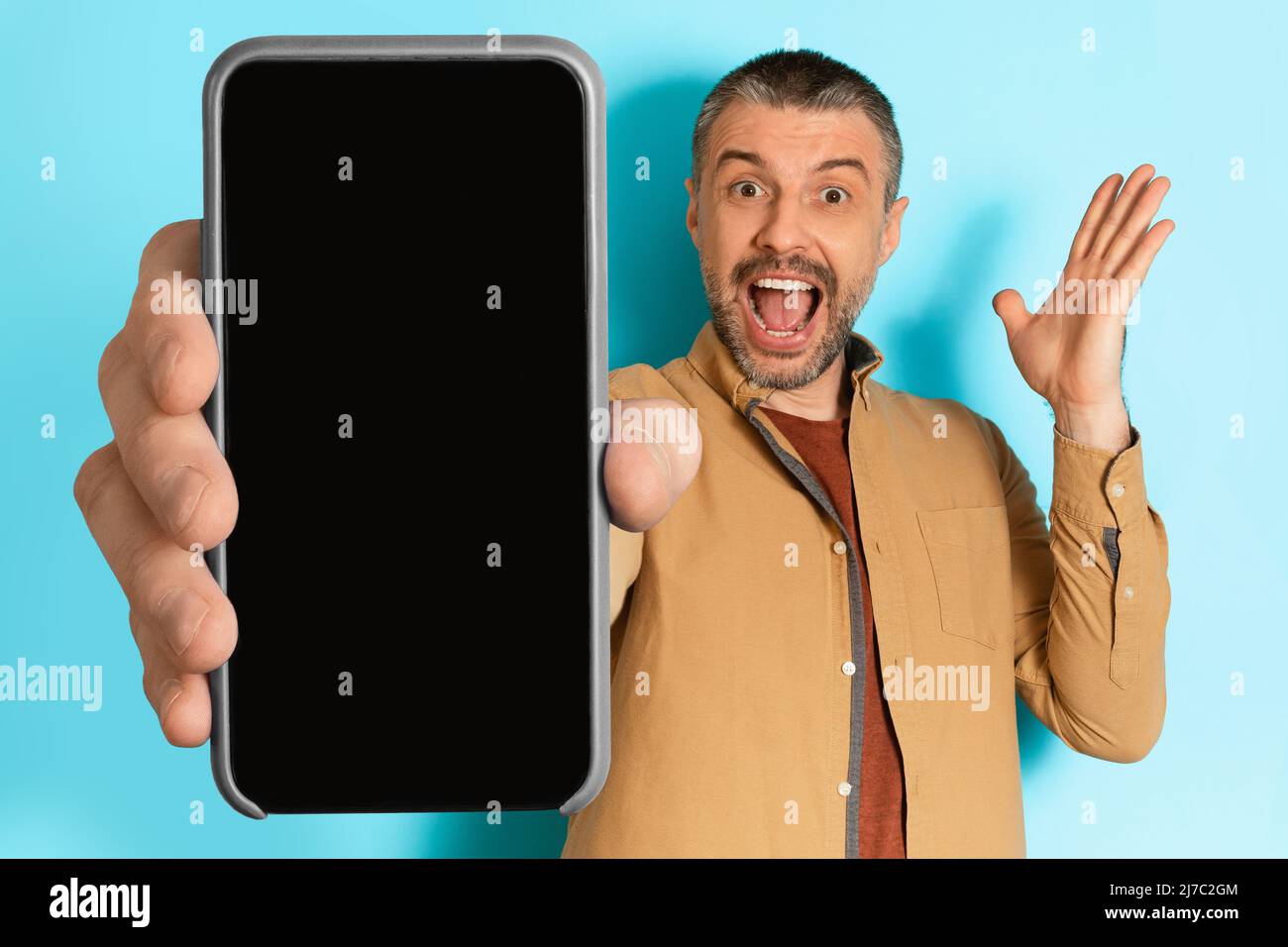L'uomo eccitato mostra lo schermo del telefono vuoto che urla su sfondo blu Foto Stock