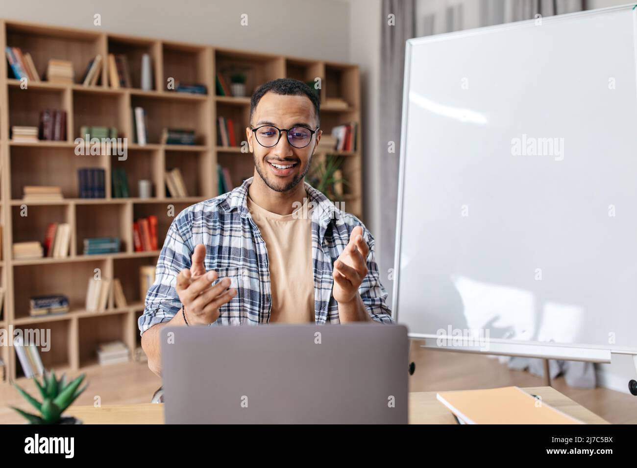 Felice maschio manager arabo seduto vicino a lavagna vuota e spiegare la nuova strategia aziendale ai colleghi Foto Stock