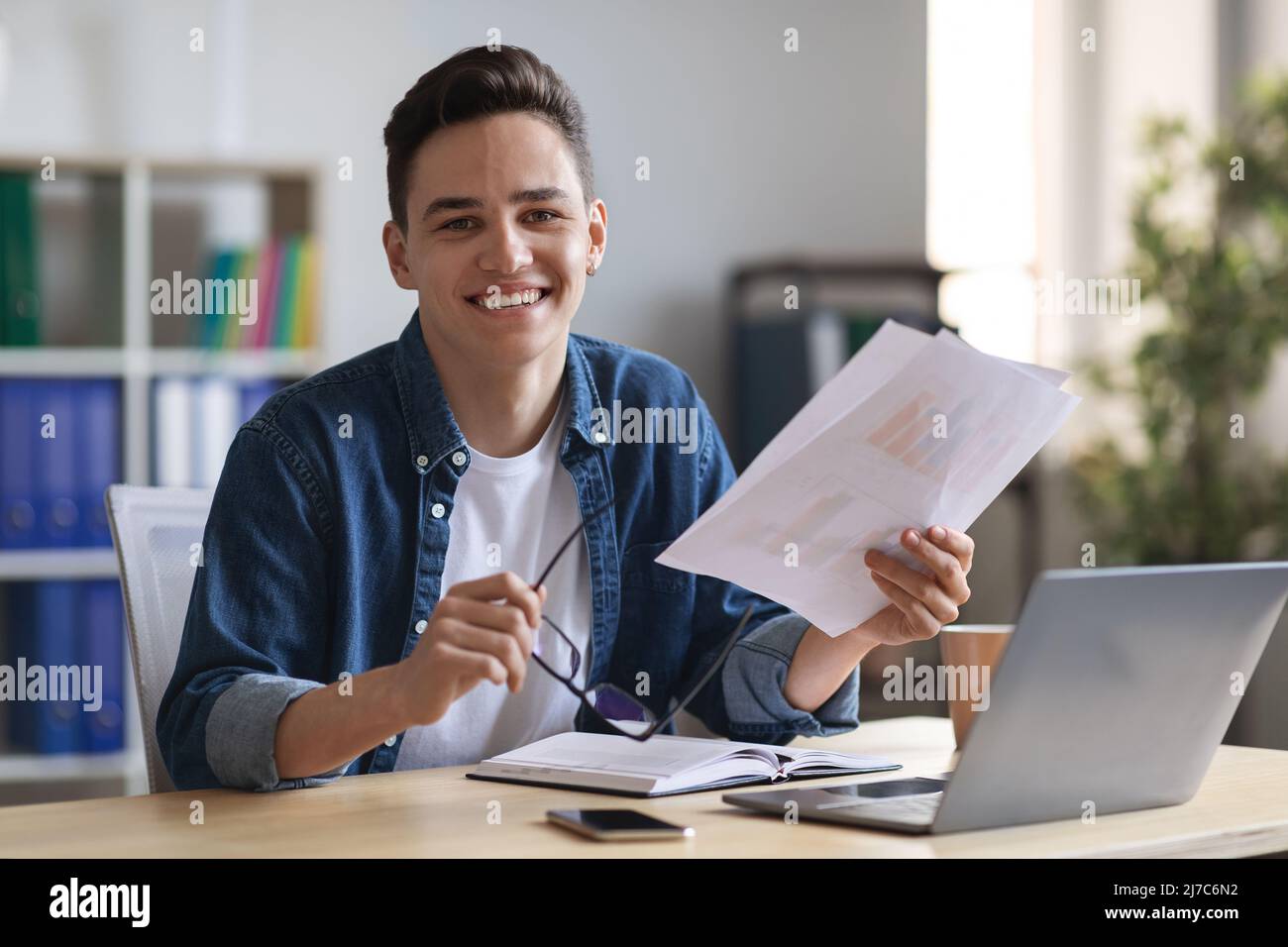 Giovane uomo sorridente imprenditore che lavora con documenti alla scrivania in ufficio Foto Stock