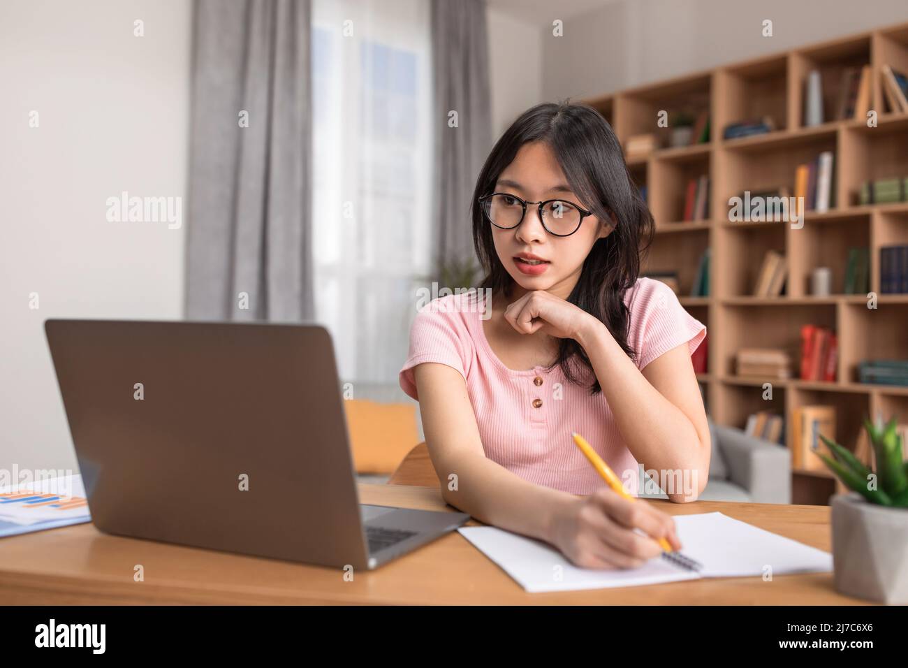 Concetto di formazione a distanza. Ritratto di donna coreana focalizzata seduta alla scrivania, utilizzando il computer portatile e scrivere in notebook Foto Stock