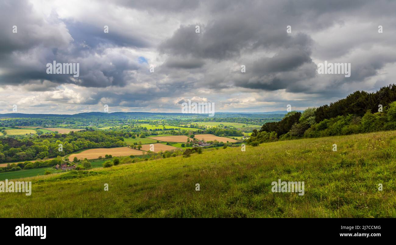 Vista della campagna a Blatchford Down, Abinger Hammer nella Surrey Hills Area of Outstanding Natural Beauty, il sole nella valle, le nuvole buie tempestose Foto Stock