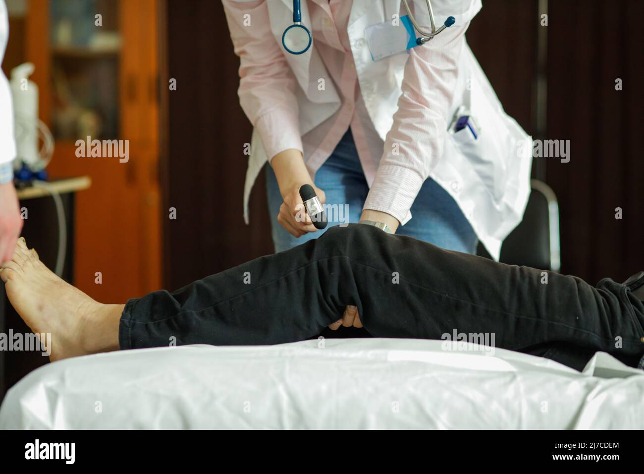 Dettagli con le mani di una giovane medica femminile che esamina i riflessi del ginocchio di un paziente. Foto Stock