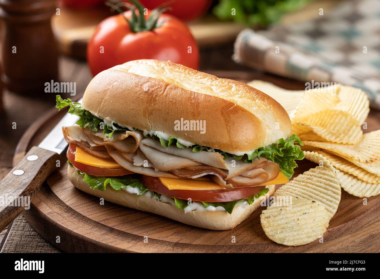 Panino a base di tacchino, lattuga, formaggio e pomodoro su una panna con pomodori e lattuga sullo sfondo Foto Stock