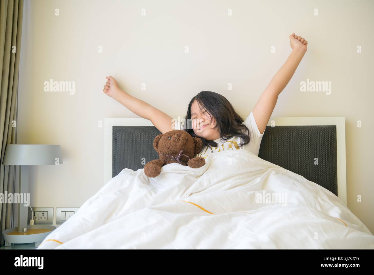 La ragazza asiatica piccola si sveglia e si allunga a letto in mattina, l'assistenza sanitaria e il buon concetto del mondo del mattino Foto Stock