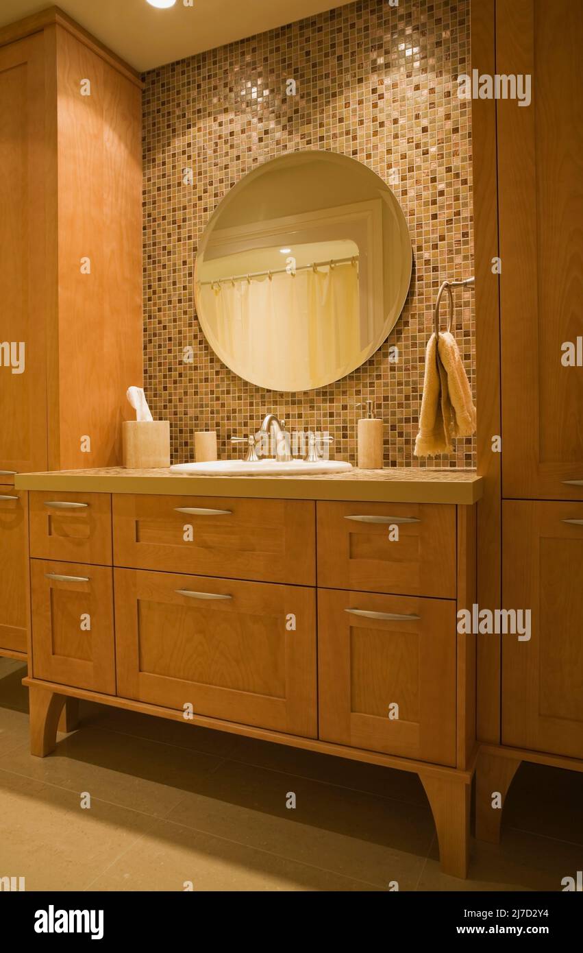Grande specchio rotondo incorniciato da vanity in legno nella stanza da bagno degli ospiti all'interno di una lussuosa casa. Foto Stock