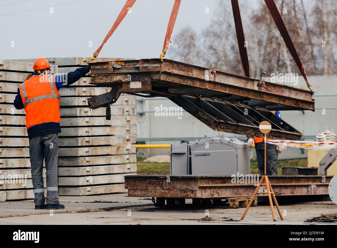 L'imbragatura in casco e gilet controlla lo scarico di strutture metalliche in cantiere. Il manichino bianco scarica il carico. Foto Stock