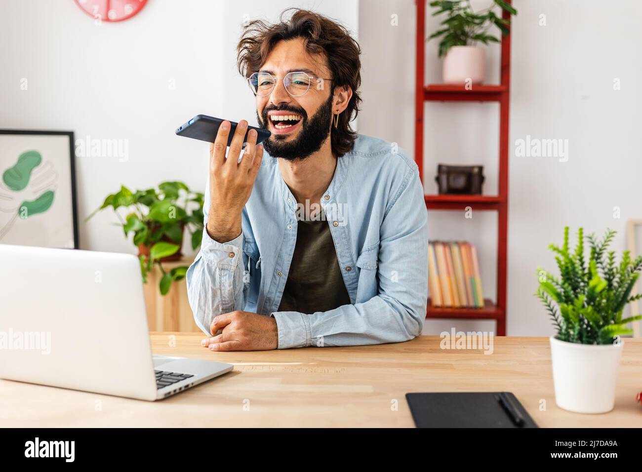 Felice uomo giovane sorridente mentre invia un messaggio vocale sul cellulare a casa Foto Stock