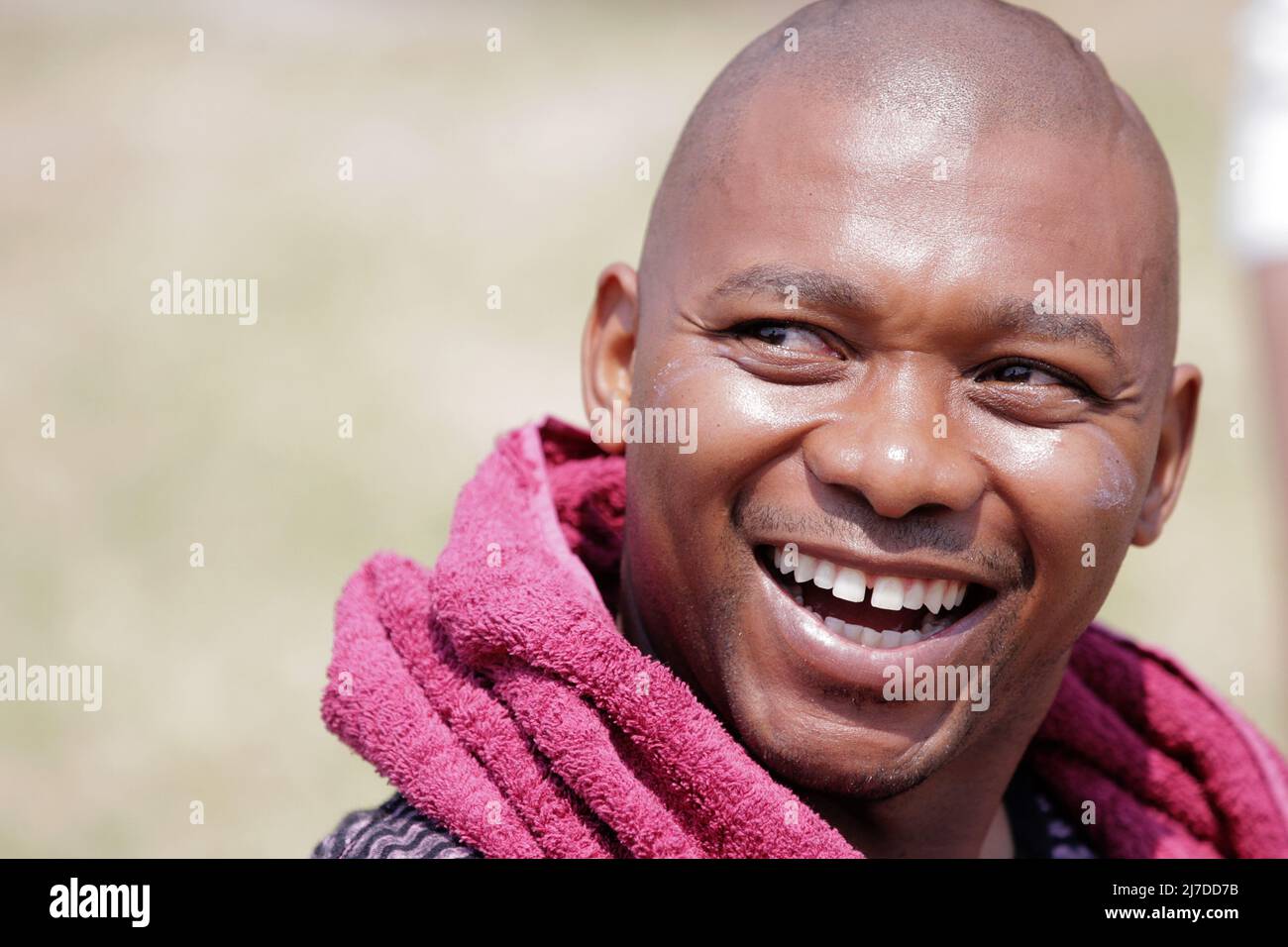 Studente nero sorridente all'evento di team-building GSB, asciugamano rosa avvolto intorno al collo, sfondo sfocato. Foto Stock