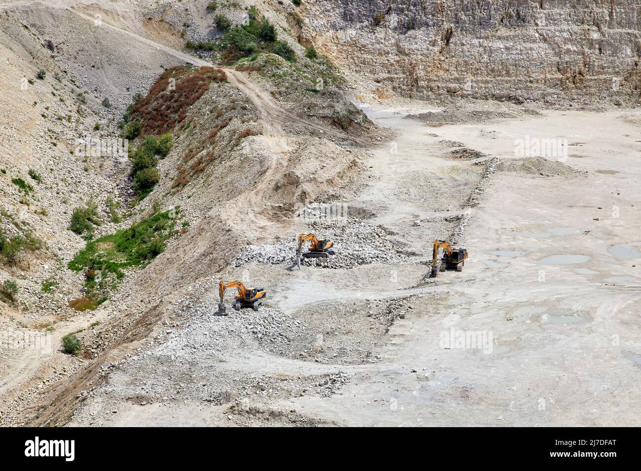 Tre escavatori scavano una pietra sul fondo di una grande cava Foto Stock