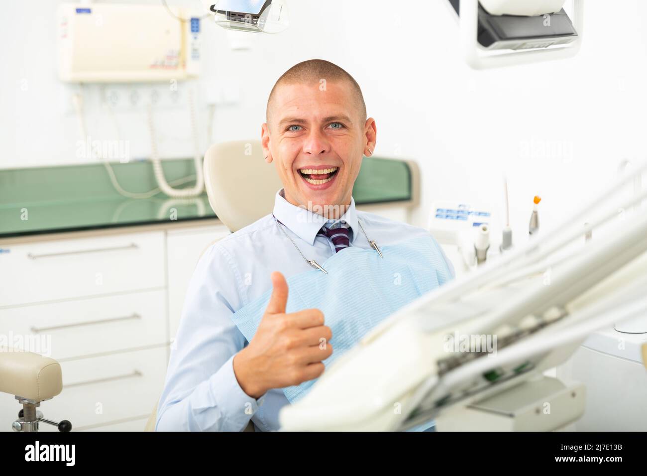 Paziente di sesso maschile che mostra il pollice in su dopo il trattamento dentale in clinica Foto Stock