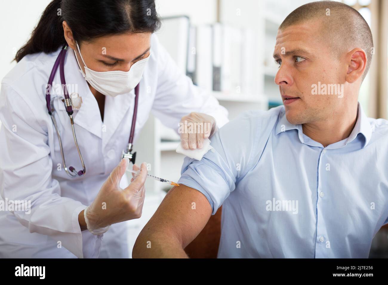 Medico in maschera che dà il vaccino al pacient in ufficio Foto Stock