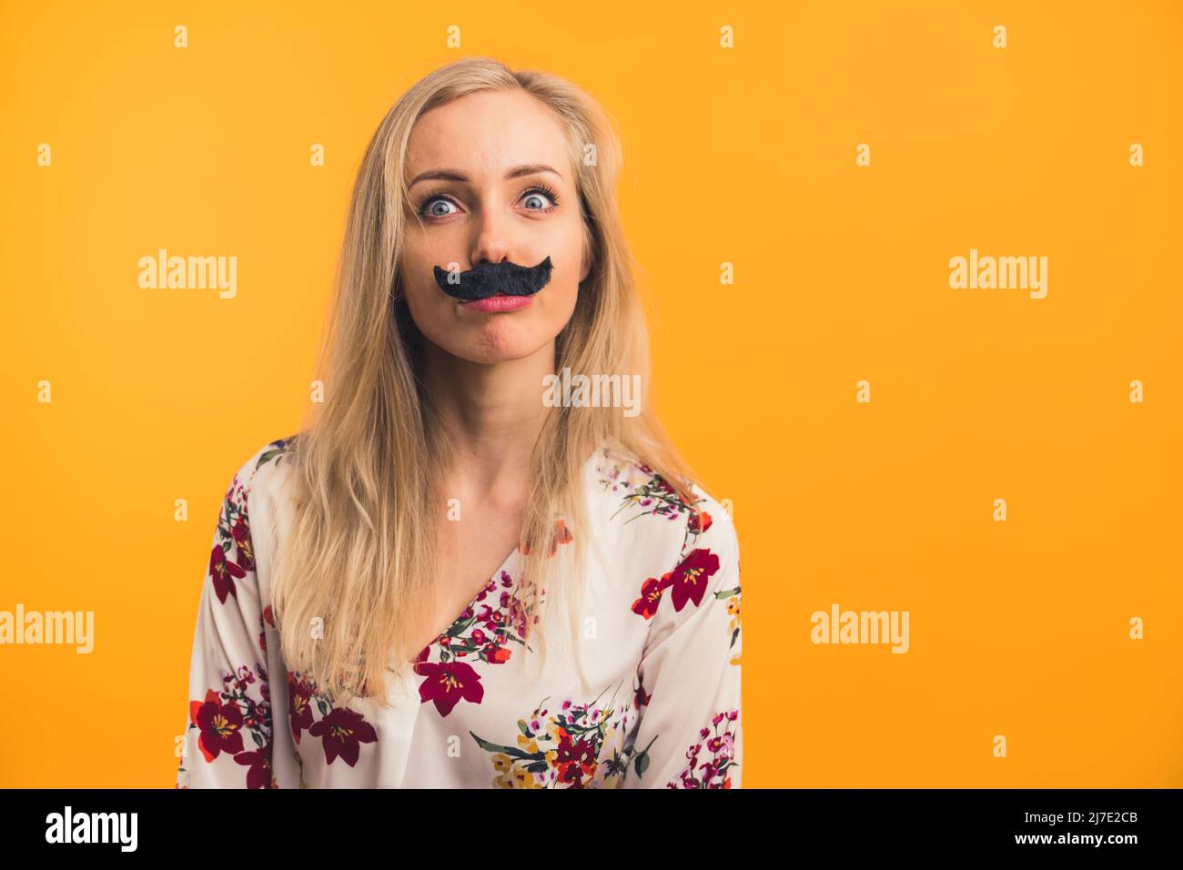 Studio girato giovane donna bionda con falsi baffi sul suo viso isolato arancione sfondo copia spazio al chiuso . Foto di alta qualità Foto Stock