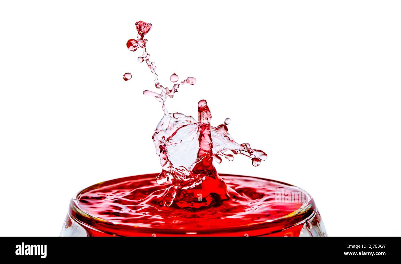 Scatto macro di una caduta collisione in un bicchiere di acqua rossa. Foto Stock