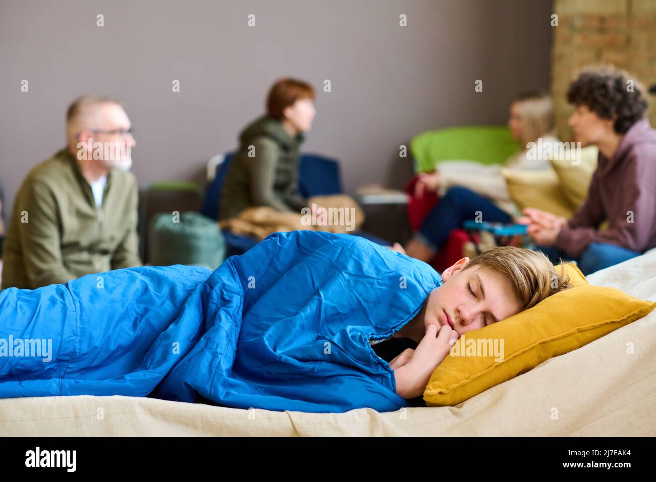 Carino ragazzo sereno con la testa su cuscino che dorme sotto coperta su cochette contro il roup di rifugiati discutere le ultime notizie Foto Stock
