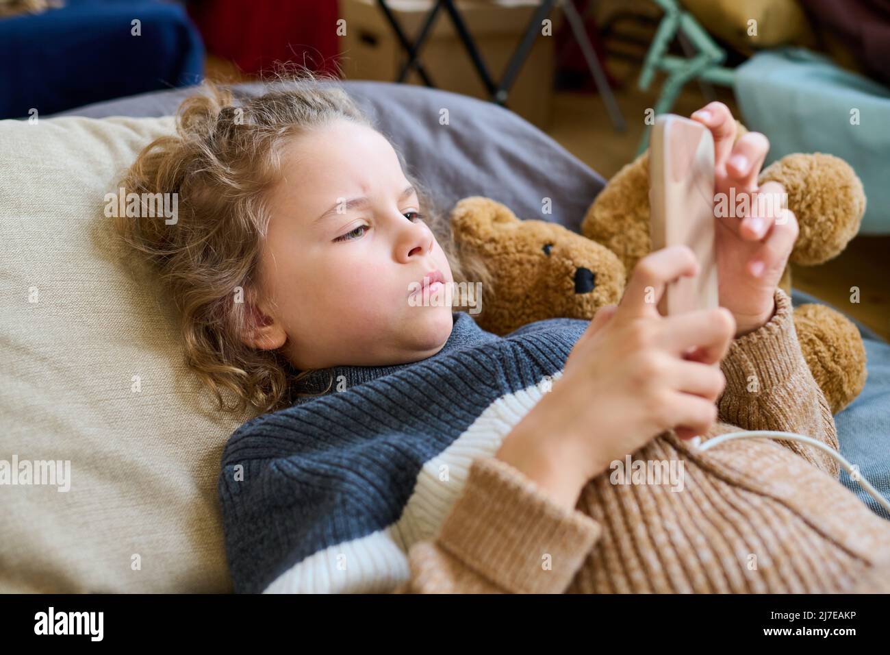 Ragazzo biondo carino in maglione casual lavorato a maglia sdraiato sulla cuchette e scorrere nel suo cellulare mentre si riposa in un rifugio temporaneo Foto Stock