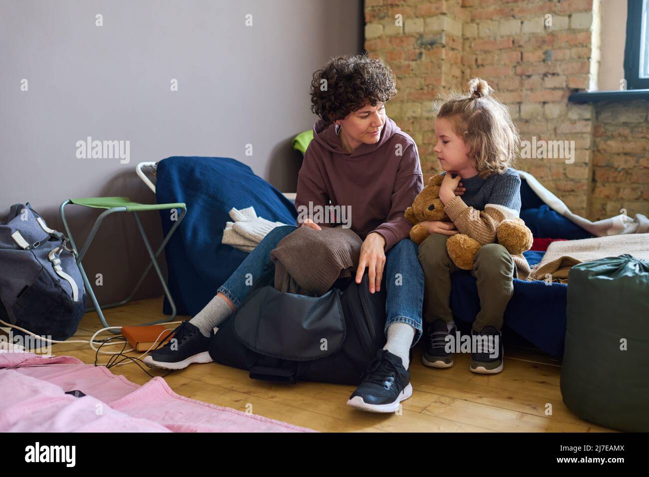 Giovane donna in casualwear che guarda suo figlio mentre si siede sulla cuchette accanto a lui e prendendo caldo maglione grigio lana fuori dalla borsa Foto Stock