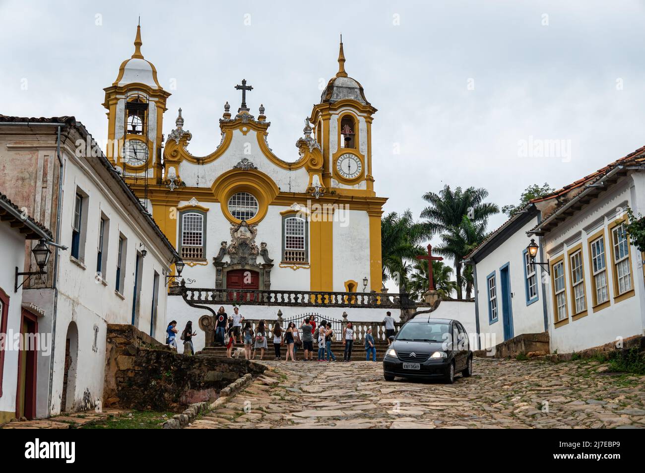 La famosa chiesa madre di Santo Antonio circondata da case coloniali in via Rua da Camara nel centro storico di Tiradentes, sotto il cielo nuvoloso. Foto Stock