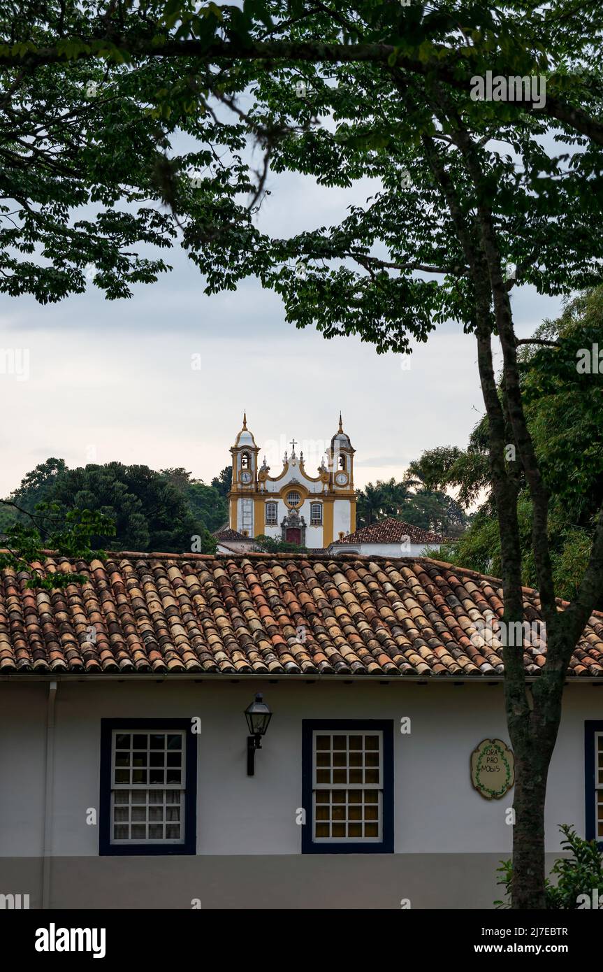 Vista distante della chiesa madre di Santo Antonio come visto da Francisco Candido Barbosa strada tra un edificio coloniale e gli alberi sotto il cielo nuvoloso. Foto Stock