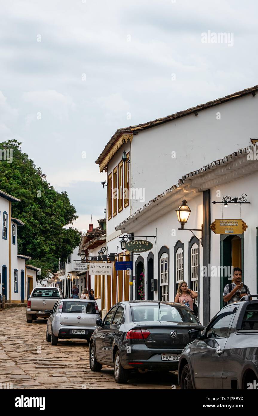 Edifici coloniali fianco a fianco si trova in Direita strada con auto parcheggiate nelle vicinanze nel centro storico di Tiradentes sotto il cielo nuvoloso. Foto Stock
