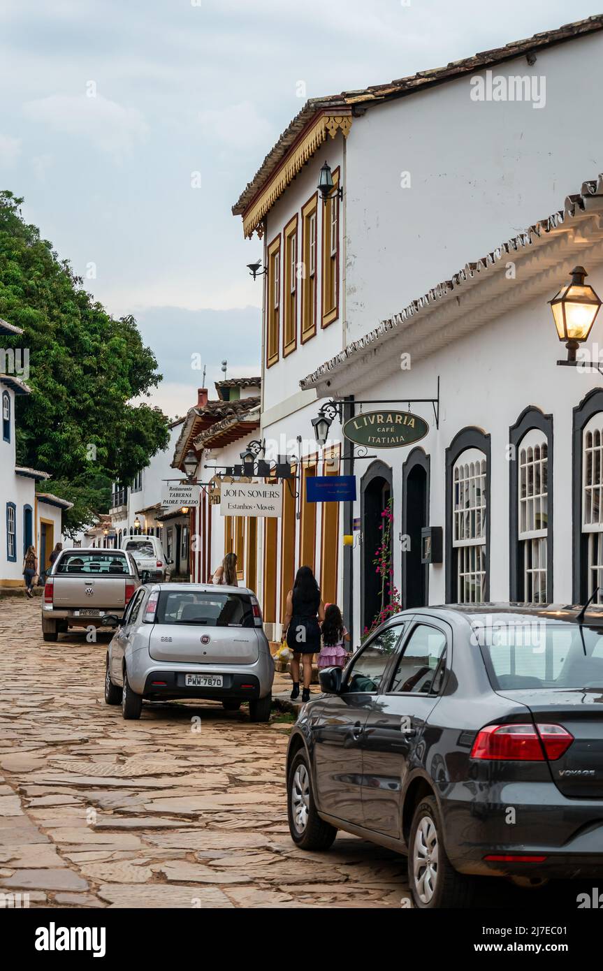 Edifici coloniali fianco a fianco si trova in Direita strada con auto parcheggiate nelle vicinanze nel centro storico di Tiradentes sotto il cielo nuvoloso. Foto Stock