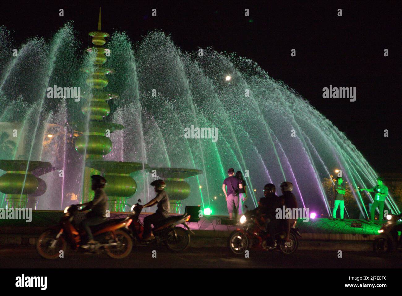 Le persone che si divertono presso una fontana, in primo piano del traffico stradale serale a Palembang, Sumatra meridionale, Indonesia. Foto Stock