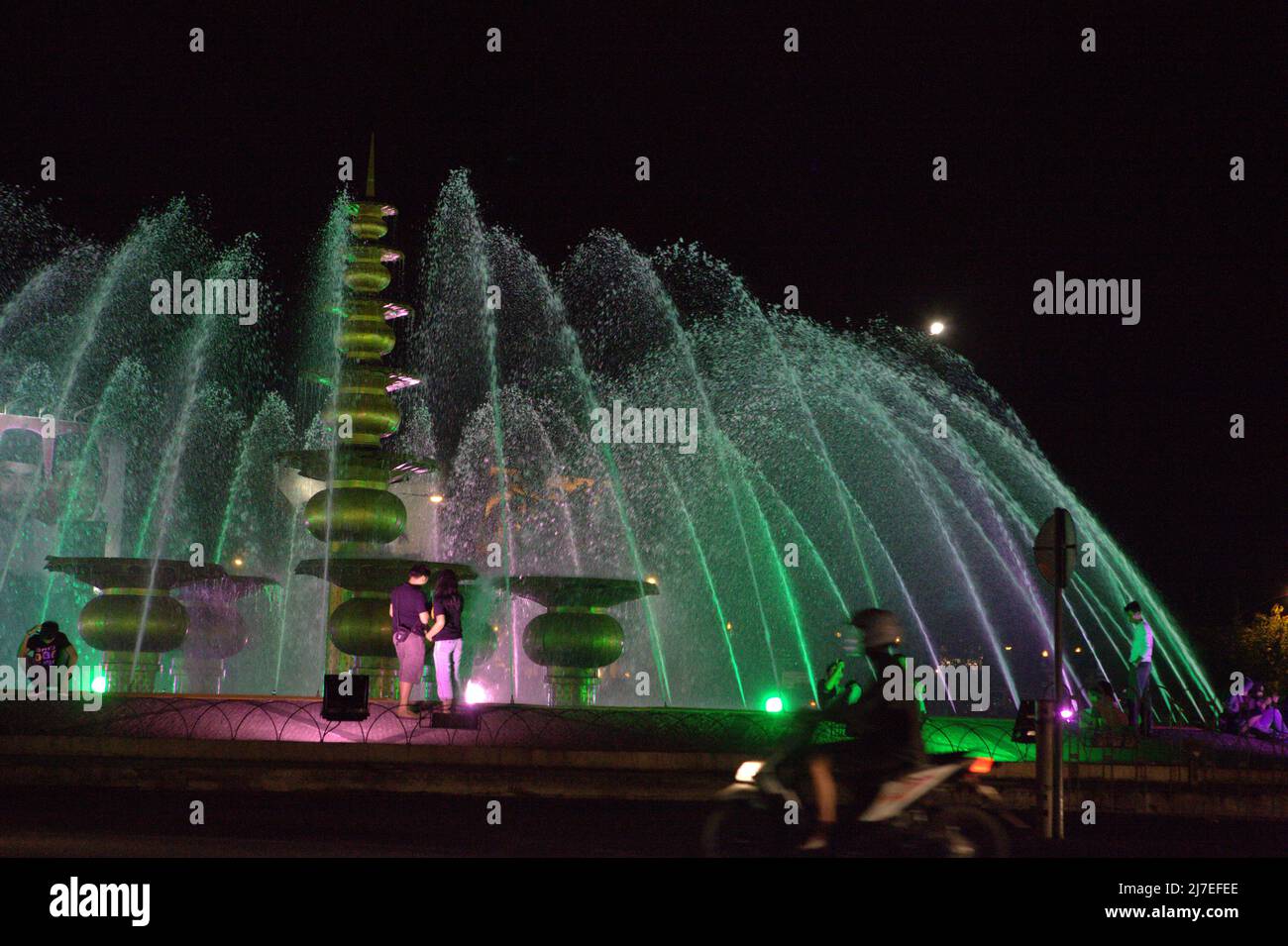 Le persone che si divertono presso una fontana, in primo piano del traffico stradale serale a Palembang, Sumatra meridionale, Indonesia. Foto Stock