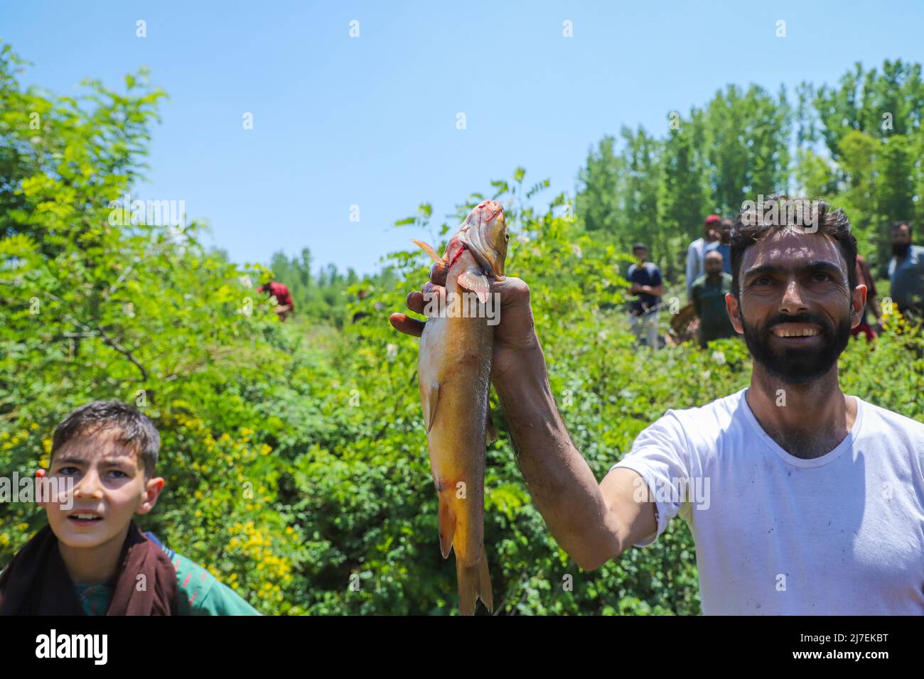 L'uomo di Kashmiri tiene un pesce durante un festival annuale di pulizia e pesca nel distretto di Anantnag del Kashmir del sud. Ogni anno nel mese di maggio, centinaia di abitanti del villaggio prendono un giorno fuori per partecipare ad un festival di pesca e di pulizia che sta andando avanti per le età. Prima di arare le risaie, l'attività matura la sorgente di limo e erbacce e ripristina il livello dell'acqua per il resto dell'anno. Foto Stock