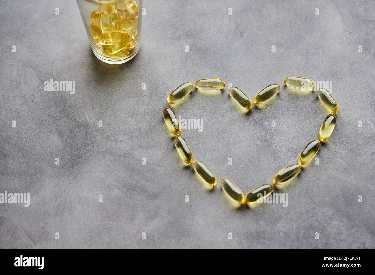 Capsule a forma di cuore omega-3 su sfondo grigio. Il concetto di medicina e di vita sana. Vista dall'alto. Foto Stock