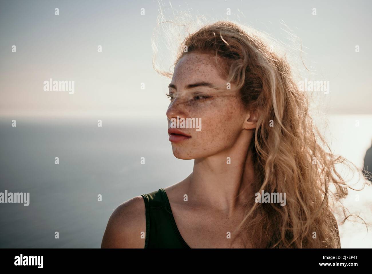 Primo piano di una bella giovane donna caucasica con capelli ricci biondi e freckles guardando la macchina fotografica e sorridendo. Cute donna ritratto in posa su un Foto Stock