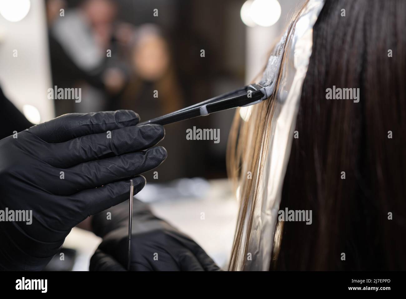 primo piano vista laterale di un filo di capelli femmina su un foglio speciale di foglio, il maestro applica la tintura per capelli con una spazzola. Il processo di evidenziazione da parte di un Foto Stock