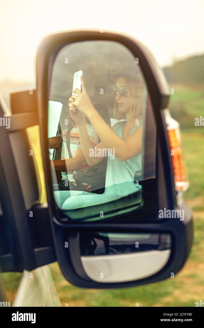 Riflessione in un camper furgone specchio retrovisore di una donna che fa una foto con il suo mobile Foto Stock