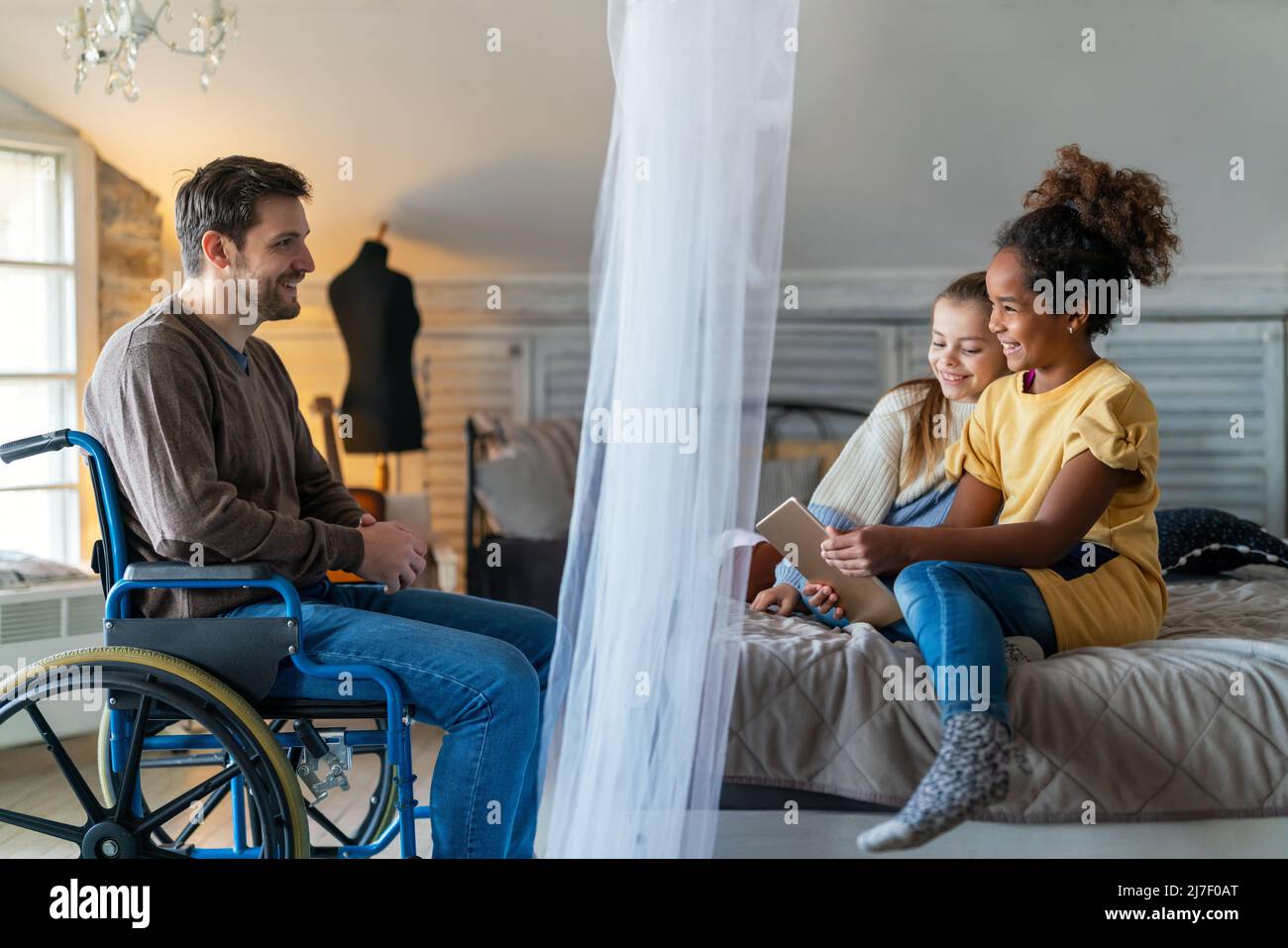 Felice padre con disabilità in sedia a rotelle godendo del tempo con i bambini a casa Foto Stock