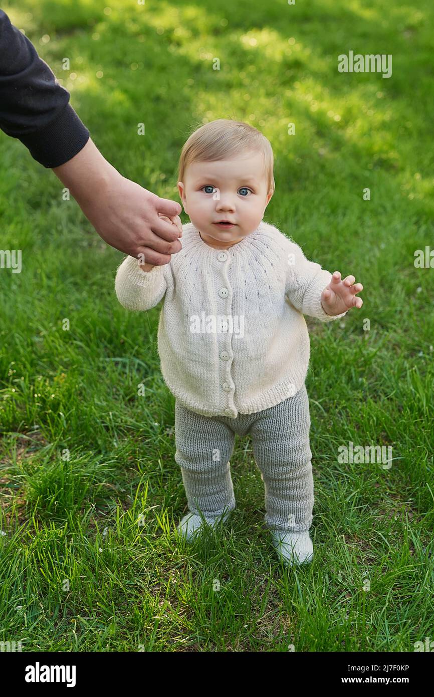 Bambino sorridente sull'erba nel parco. Giorno di protezione dei bambini. Giornata mondiale dei bambini. Il Padre tiene il bambino a mano. Primi passi. Foto Stock