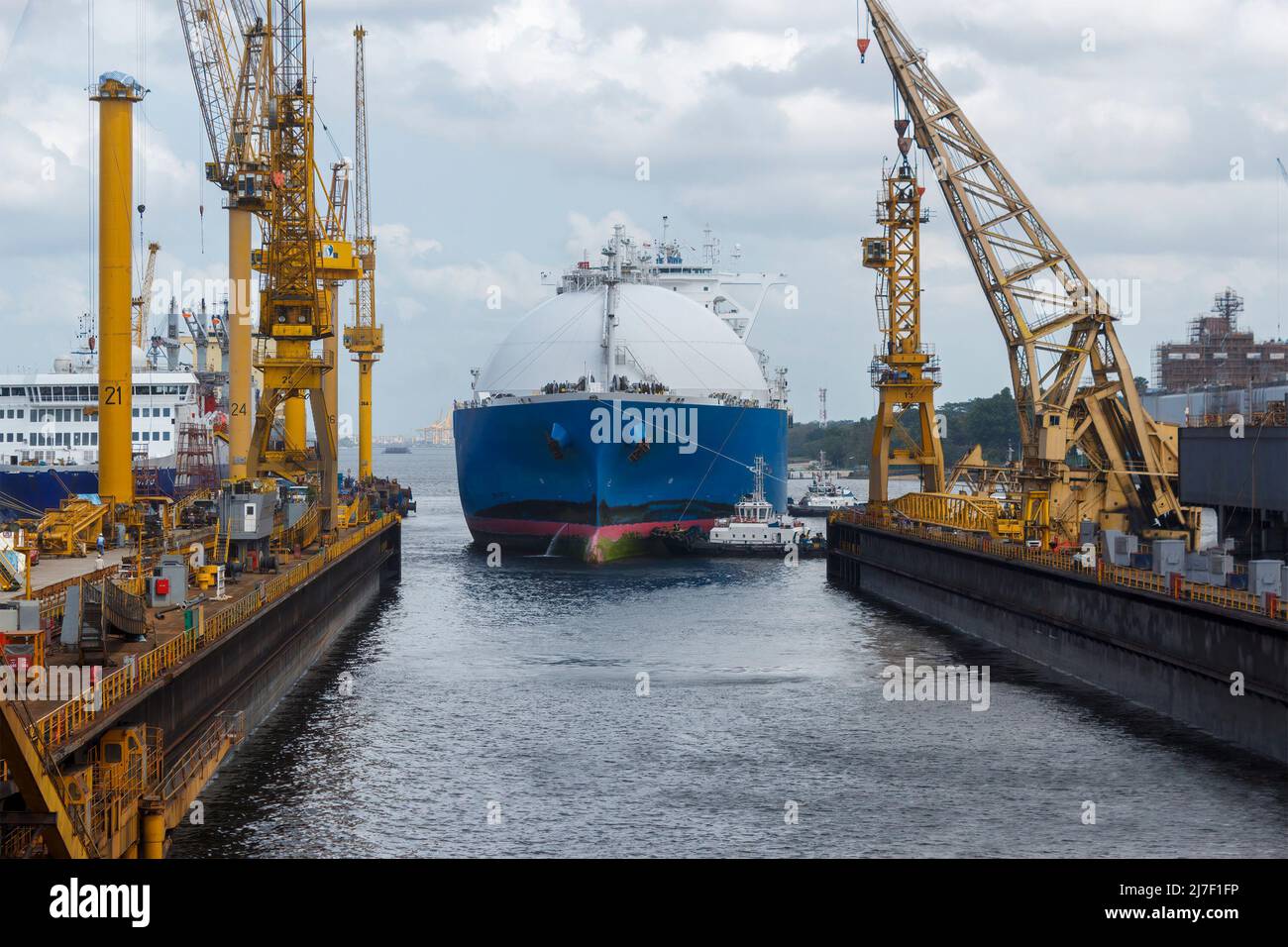 Vettore GNL che arriva in un cantiere di riparazione navale assistito da più rimorchiatori. Il bacino galleggiante viene sommerso per consentire l'inserimento dell'imbarcazione. Foto Stock