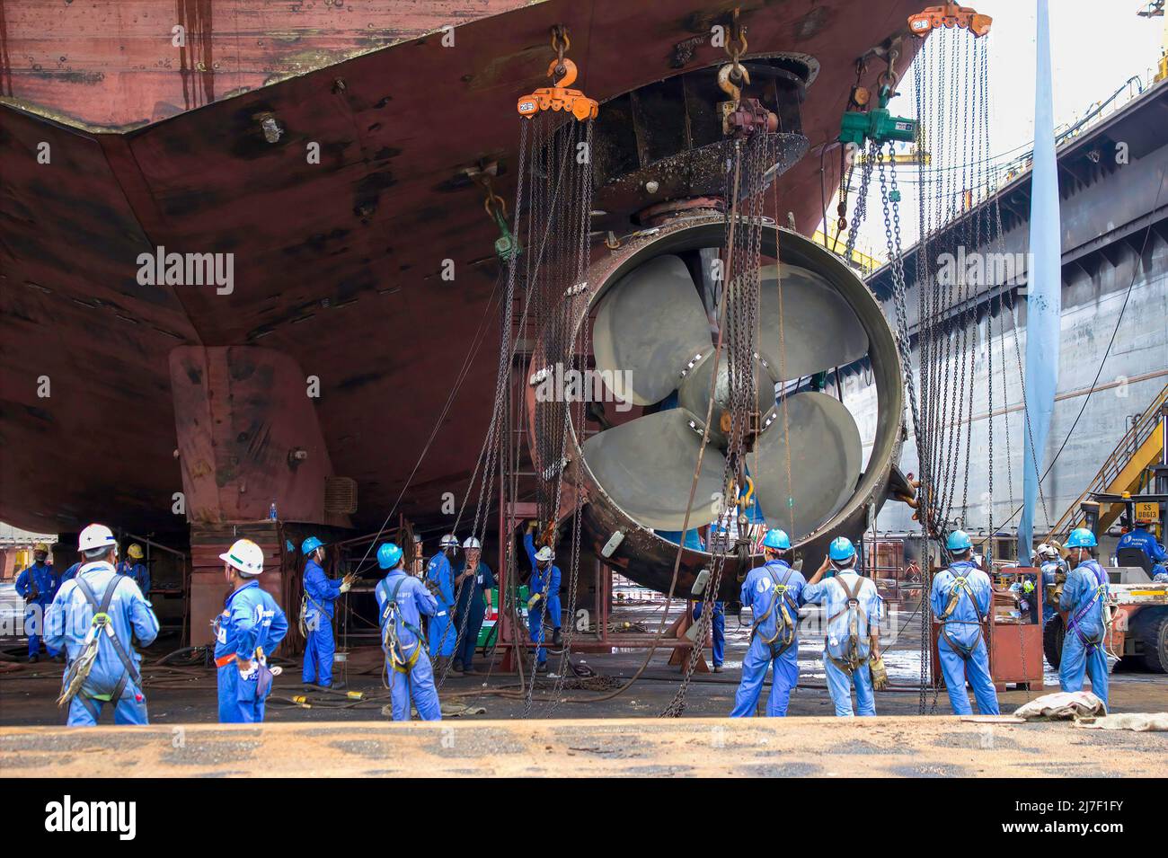 Sembawang, Singapore - Mar 2 2013: Lavoratori cantiere navale che cambiano poppa ugello azimode propulsori per nave offshore utilizzando diversi paranchi a catena Foto Stock