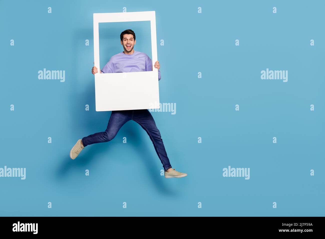 Vista a tutta lunghezza del corpo di un ragazzo allegro che salta tenendo foto finestra cornice isolata su sfondo blu brillante Foto Stock