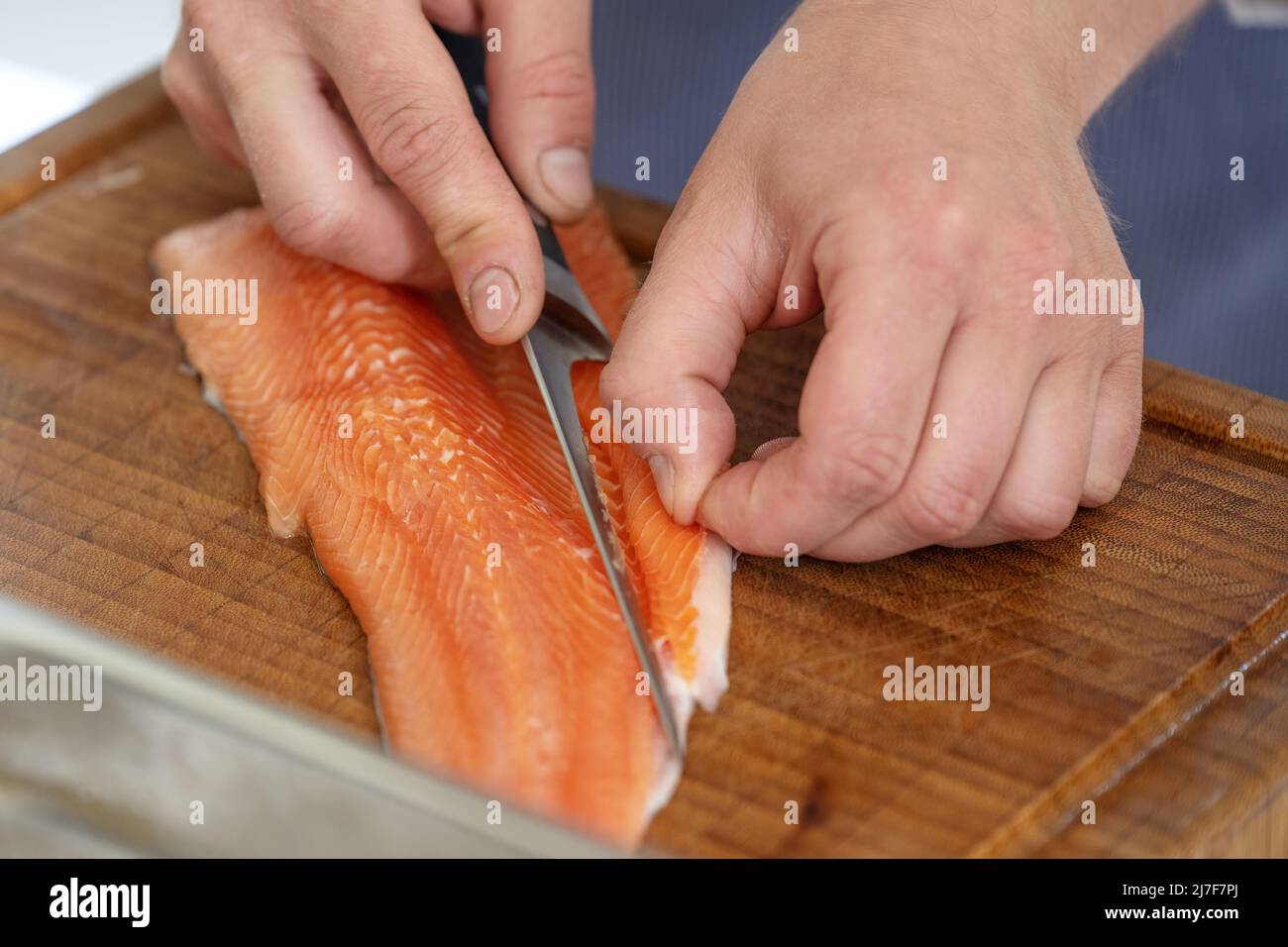 Le mani di un cuoco rimuovono il lembo della pancia con le ossa di un pesce fresco di corro crudo con un coltello di filetto su un tagliere, fuoco selezionato, profondità stretta di f Foto Stock