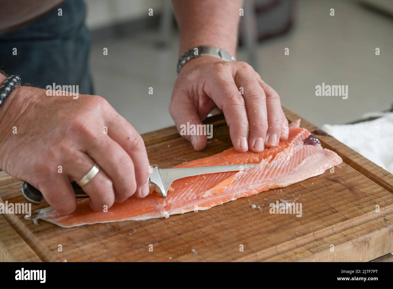 Preparazione del pesce char, cuoco sta rimuovendo le ossa con un coltello sottile di filetto su un tagliere in una cucina del ristorante, fuoco selezionato, profondità stretta Foto Stock