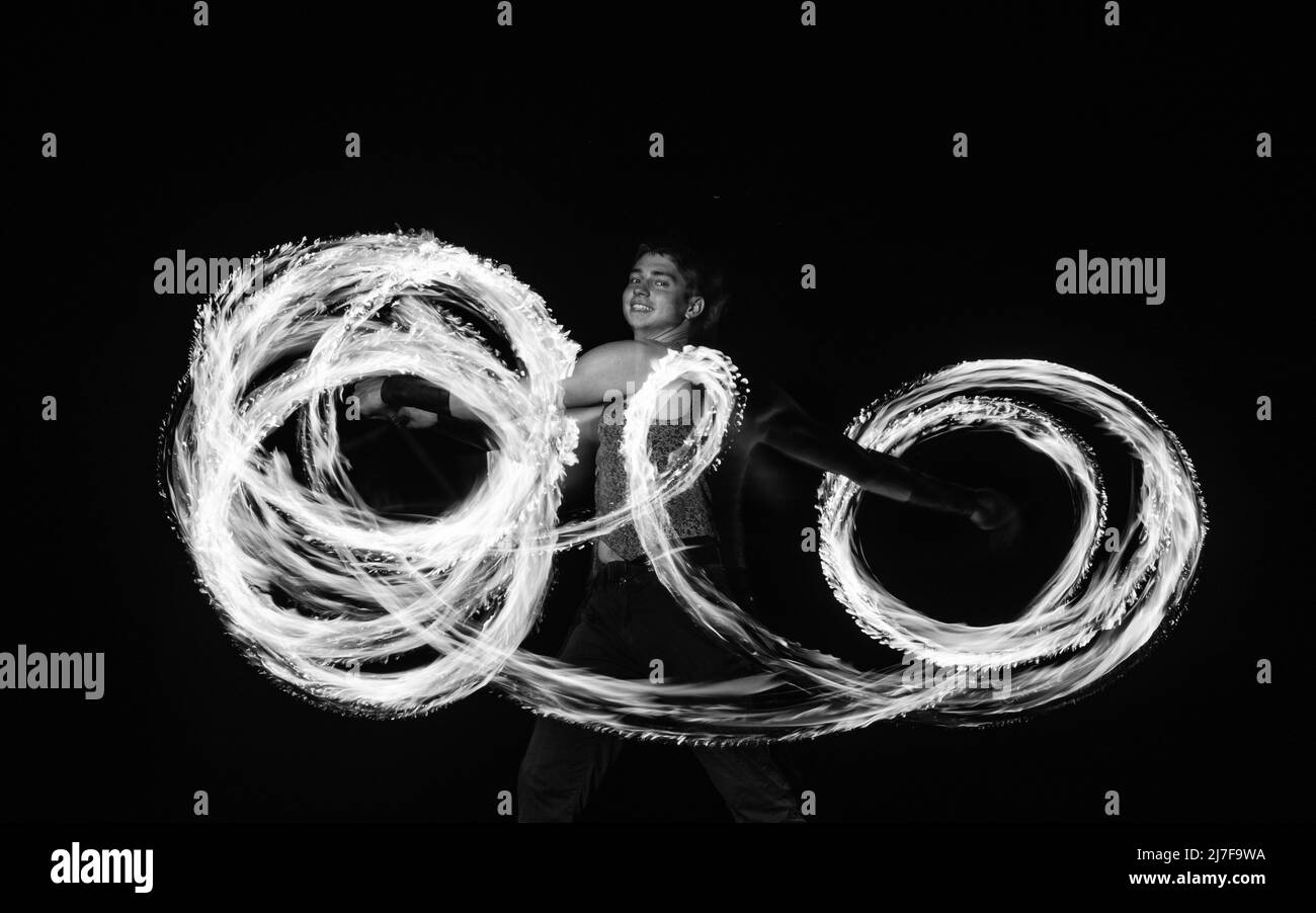 Happy maschio ballerino fuoco twirl bruciando baton creare scintillanti percorsi in movimento buio all'aperto, twirler Foto Stock