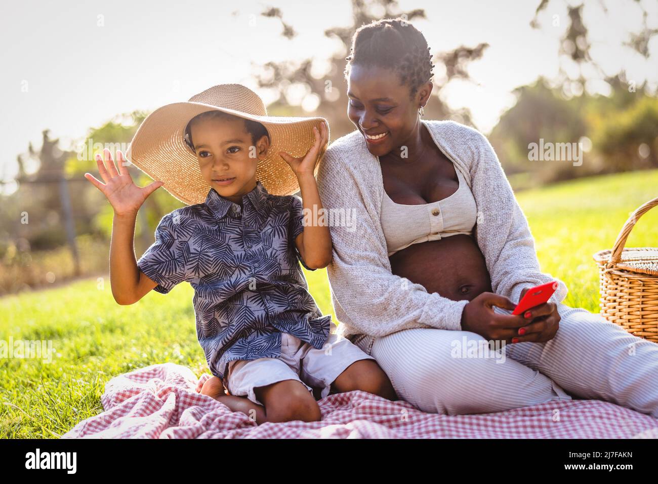 Felice madre incinta africana che passa il tempo con suo figlio fare un picnic durante il fine settimana nel parco pubblico - Maternity e genitori stile di vita concetto Foto Stock