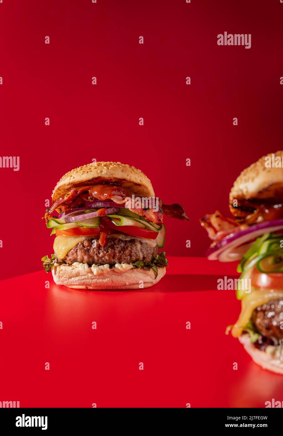 Cheeseburger fresco con lattuga, cetriolo, pomodoro, cipolla e pancetta su sfondo rosso vibrante Foto Stock